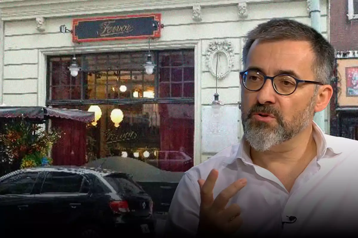 A man with a beard and glasses is speaking in front of a building with a sign and a black car parked.
