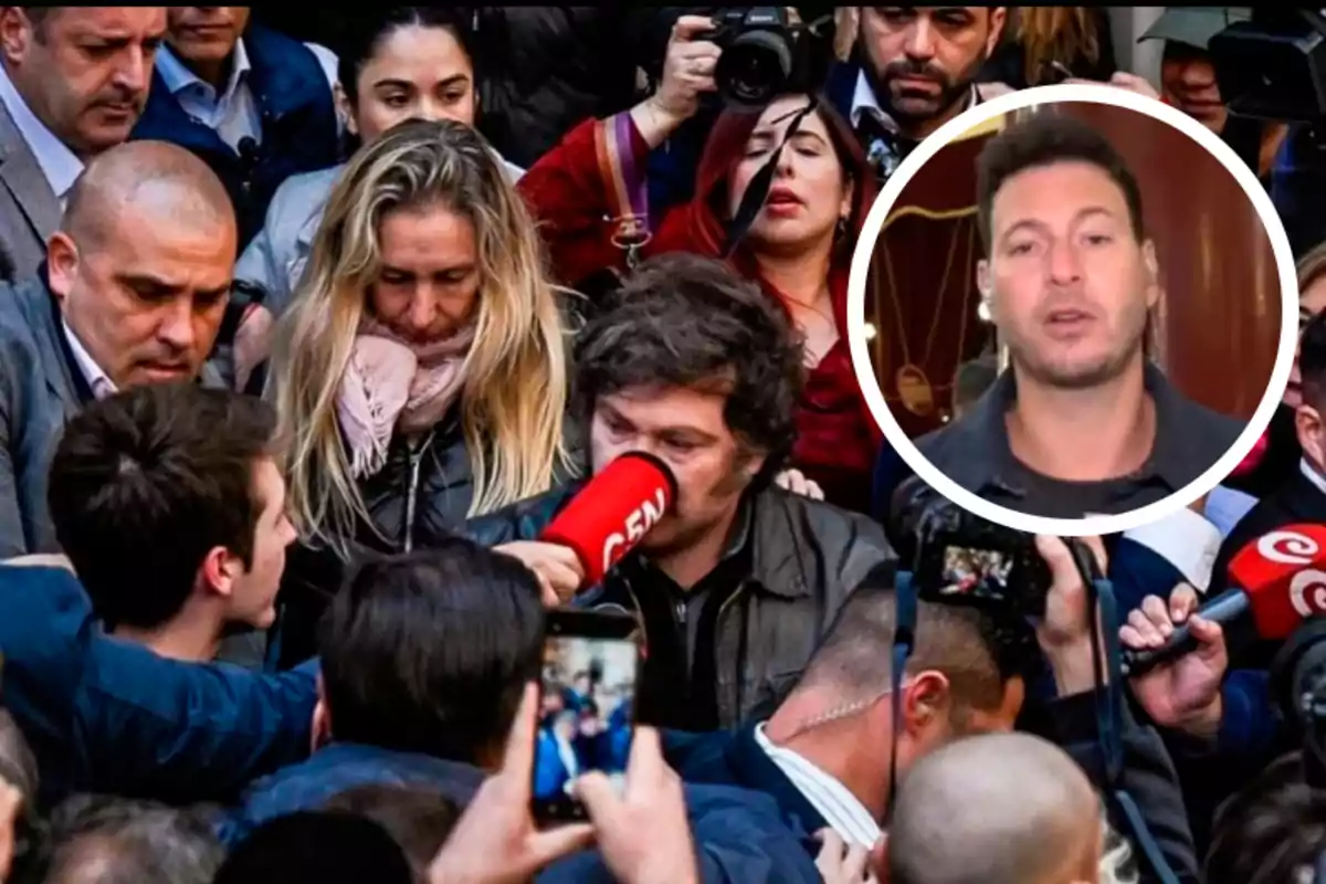 Un grupo de personas rodea a un hombre que sostiene un megáfono rojo mientras varias cámaras y micrófonos lo apuntan; en la esquina superior derecha hay un recuadro con la imagen de otra persona.