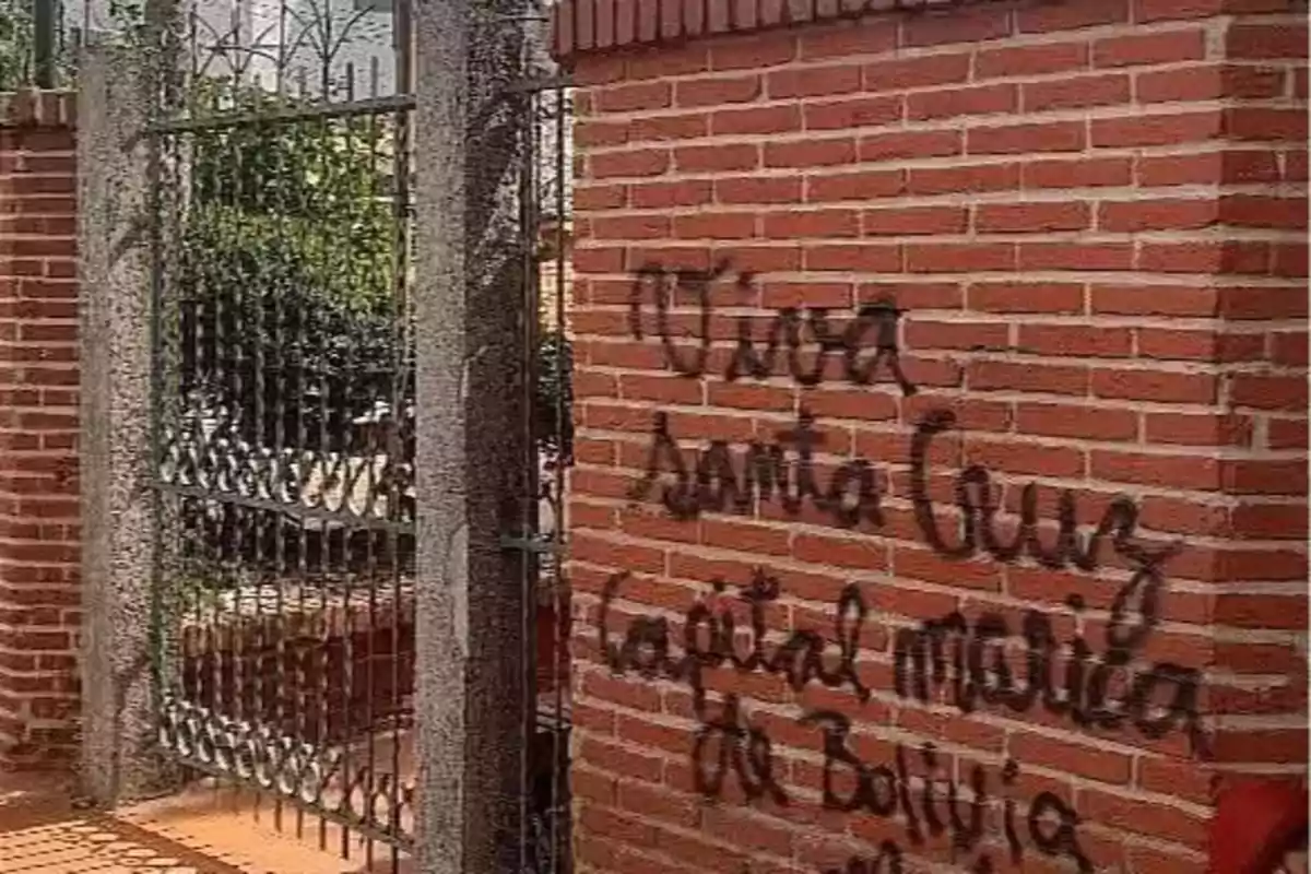 Pared de ladrillos con un grafiti en letras negras que dice Viva Santa Cruz capital moral de Bolivia junto a una reja de metal. Pared de ladrillos con un grafiti en letras negras que dice Viva Santa Cruz capital moral de Bolivia junto a una reja de metal.