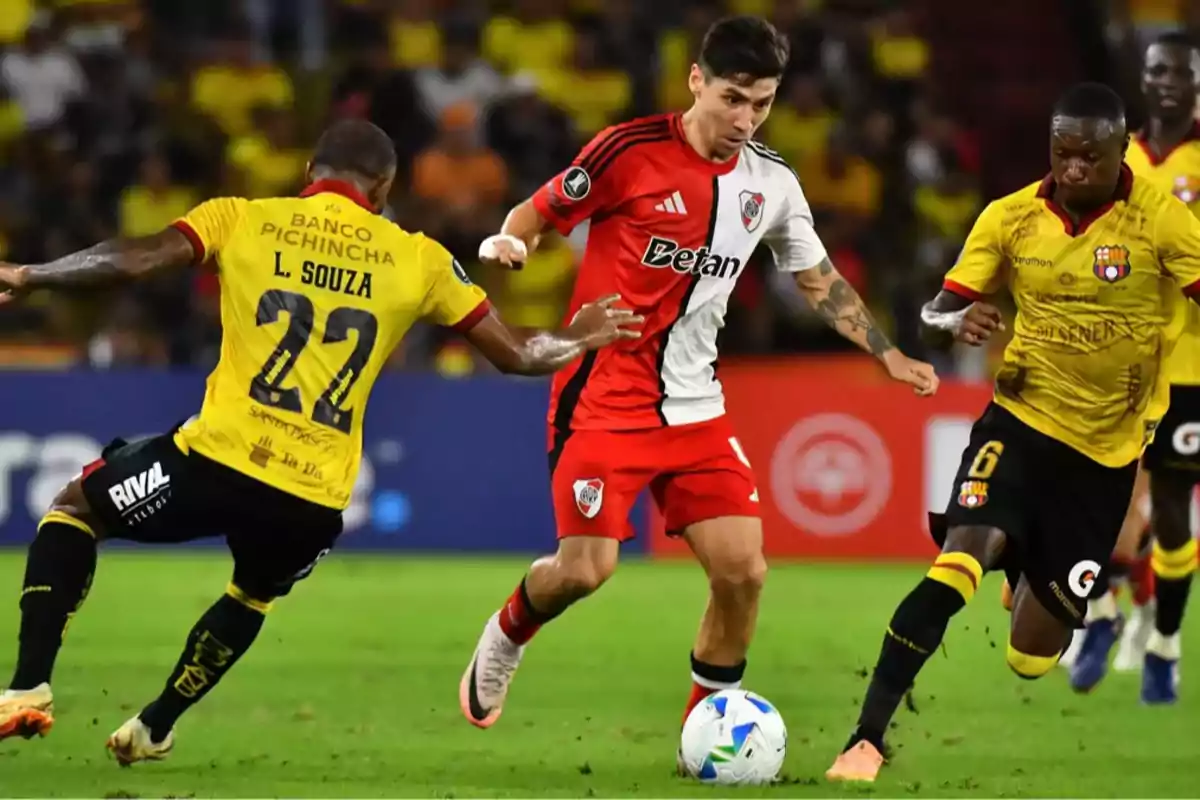 River Plate player advances with the ball while being chased by two Barcelona SC players during a soccer match.