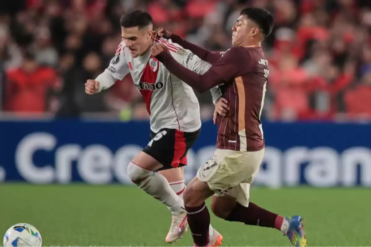 Dos futbolistas disputan el balón durante un partido en un estadio lleno de espectadores Dos futbolistas disputan el balón durante un partido en un estadio lleno de espectadores