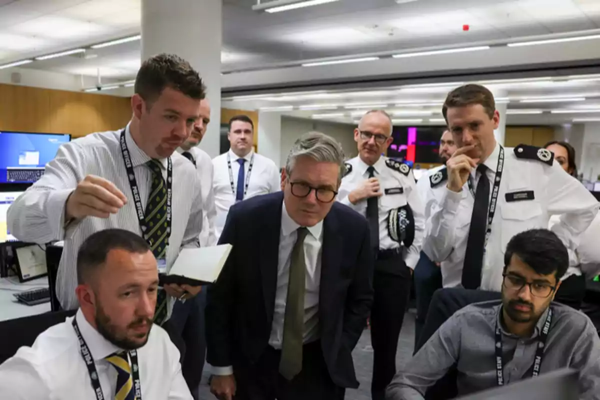 Un grupo de personas, algunas con uniformes, observan atentamente una pantalla en una oficina.