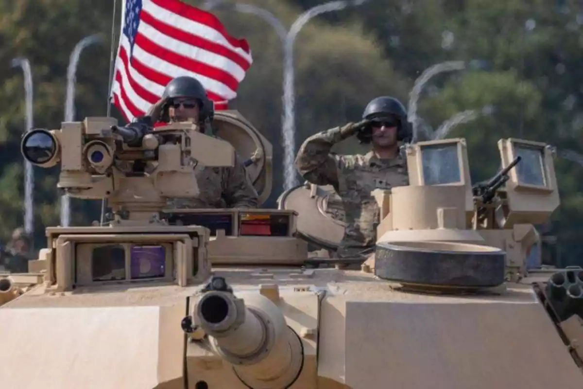 Soldados estadounidenses en uniforme militar sobre un tanque con una bandera de Estados Unidos ondeando al fondo Soldados estadounidenses en uniforme militar sobre un tanque con una bandera de Estados Unidos ondeando al fondo