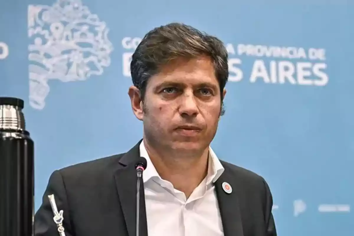 Un hombre de traje oscuro y camisa blanca está frente a un micrófono con un fondo azul que tiene texto relacionado con Buenos Aires.