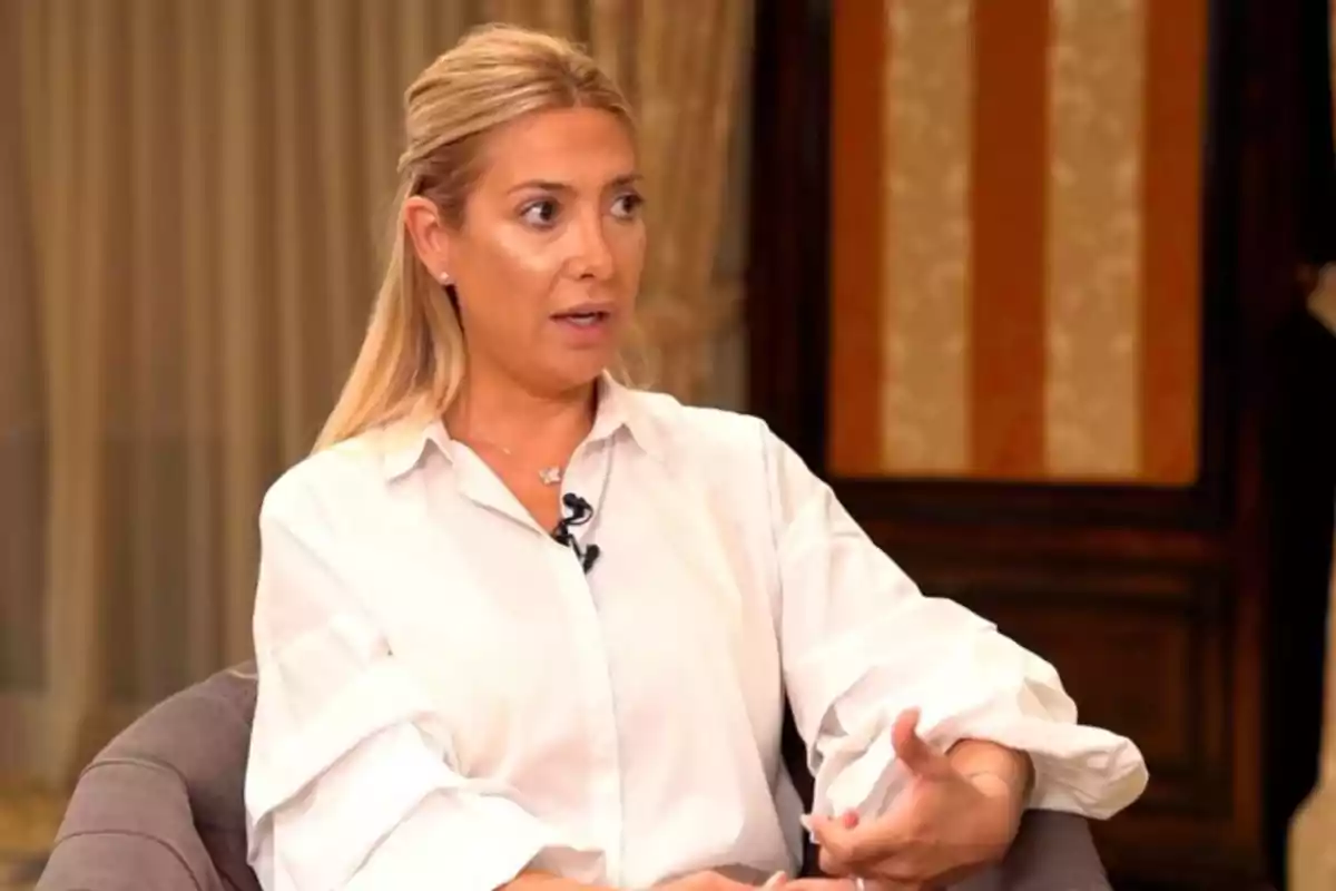 Mujer rubia con camisa blanca sentada en una silla durante una entrevista.