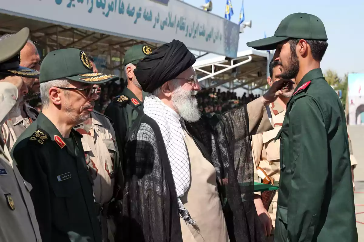Un grupo de militares iraníes con uniforme verde y beige se encuentra en formación mientras un hombre con barba y turbante negro saluda a uno de ellos en un evento al aire libre Un grupo de militares iraníes con uniforme verde y beige se encuentra en formación mientras un hombre con barba y turbante negro saluda a uno de ellos en un evento al aire libre