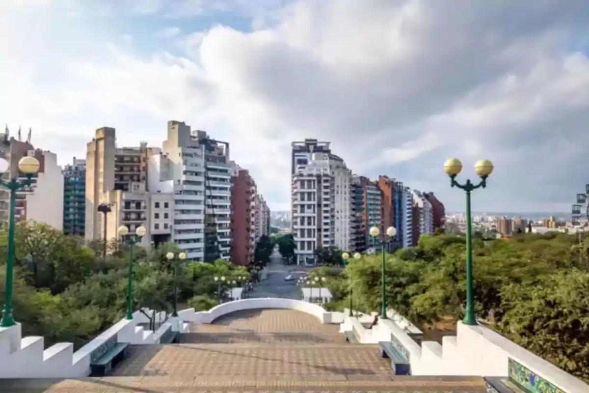Vista de una ciudad con edificios altos al fondo, árboles a los costados y una escalinata amplia con farolas verdes en primer plano Vista de una ciudad con edificios altos al fondo, árboles a los costados y una escalinata amplia con farolas verdes en primer plano