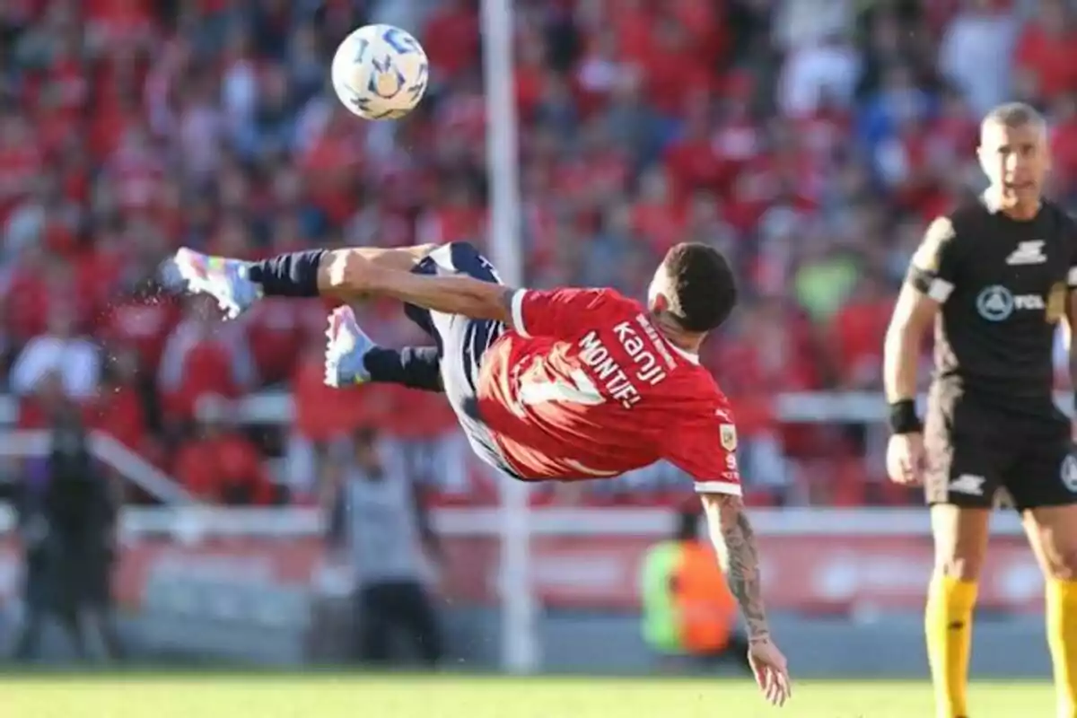 Un jugador de fútbol realiza una chilena en un partido mientras un árbitro observa. Un jugador de fútbol realiza una chilena en un partido mientras un árbitro observa.
