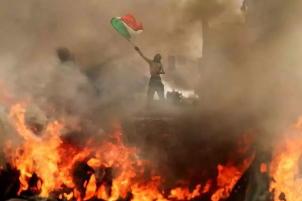 Persona ondeando una bandera en medio de humo y llamas durante una protesta