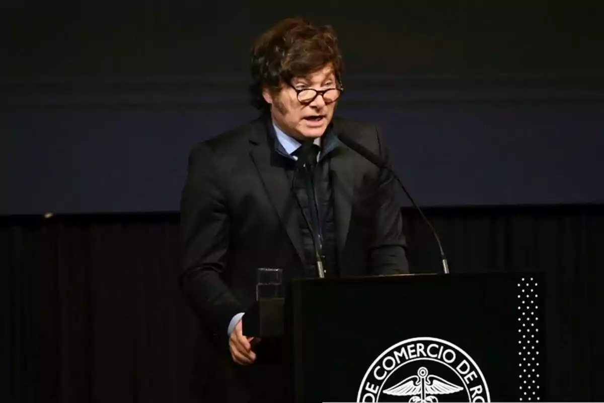 Un hombre con gafas y traje oscuro habla en un podio durante un evento.