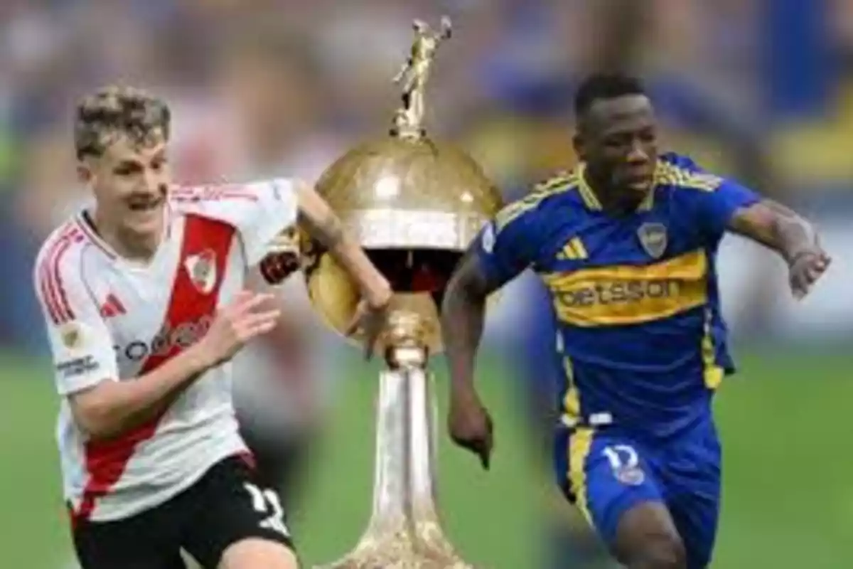 Dos futbolistas de equipos rivales corren junto a un trofeo dorado.