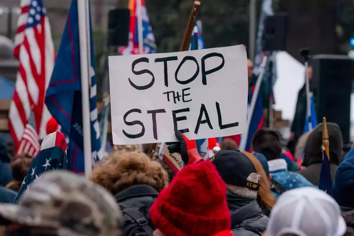 Una multitud sostiene un cartel que dice "Stop the Steal" en una manifestación con banderas estadounidenses.