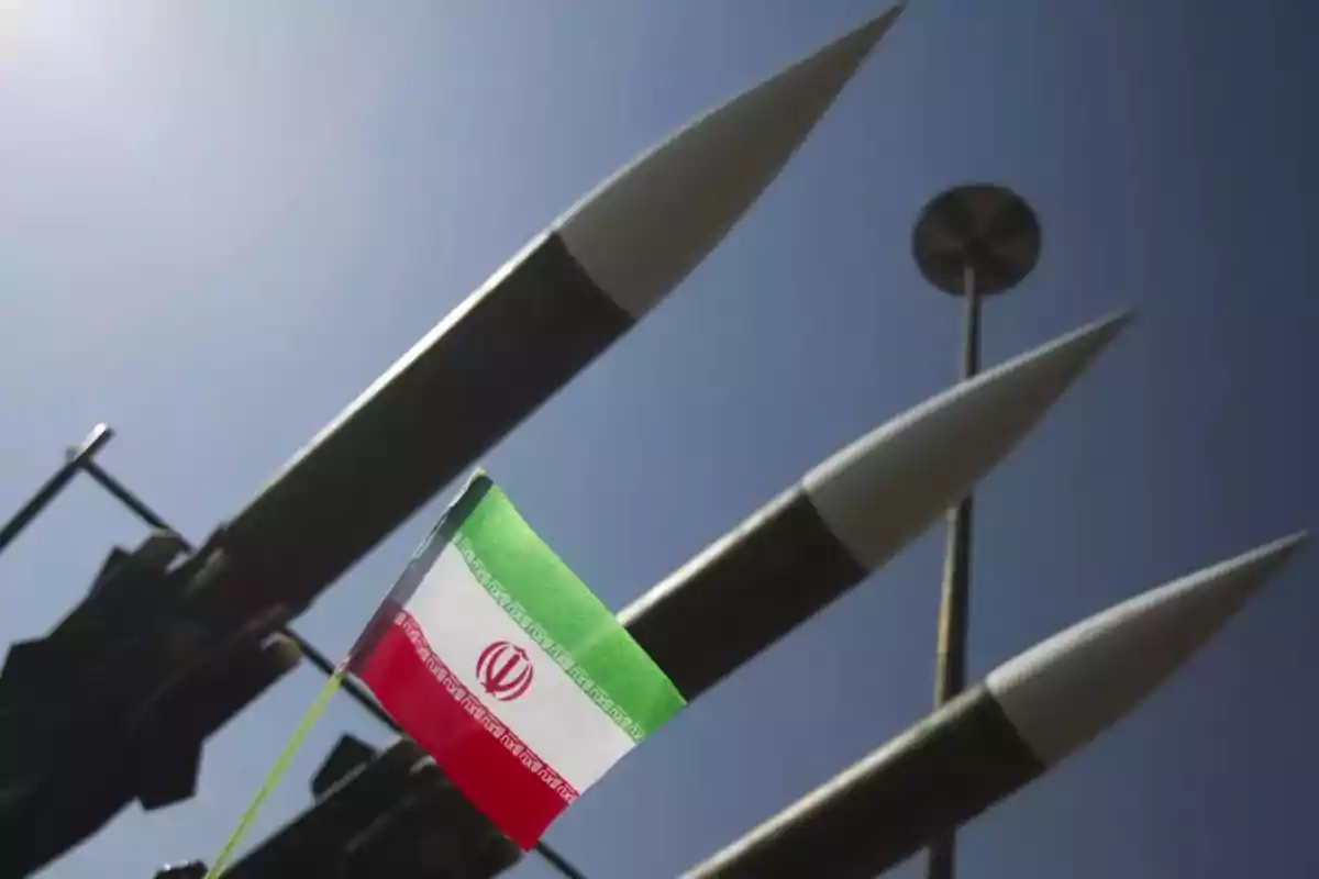 Tres misiles apuntando hacia arriba con una bandera de Irán en primer plano bajo un cielo despejado Tres misiles apuntando hacia arriba con una bandera de Irán en primer plano bajo un cielo despejado