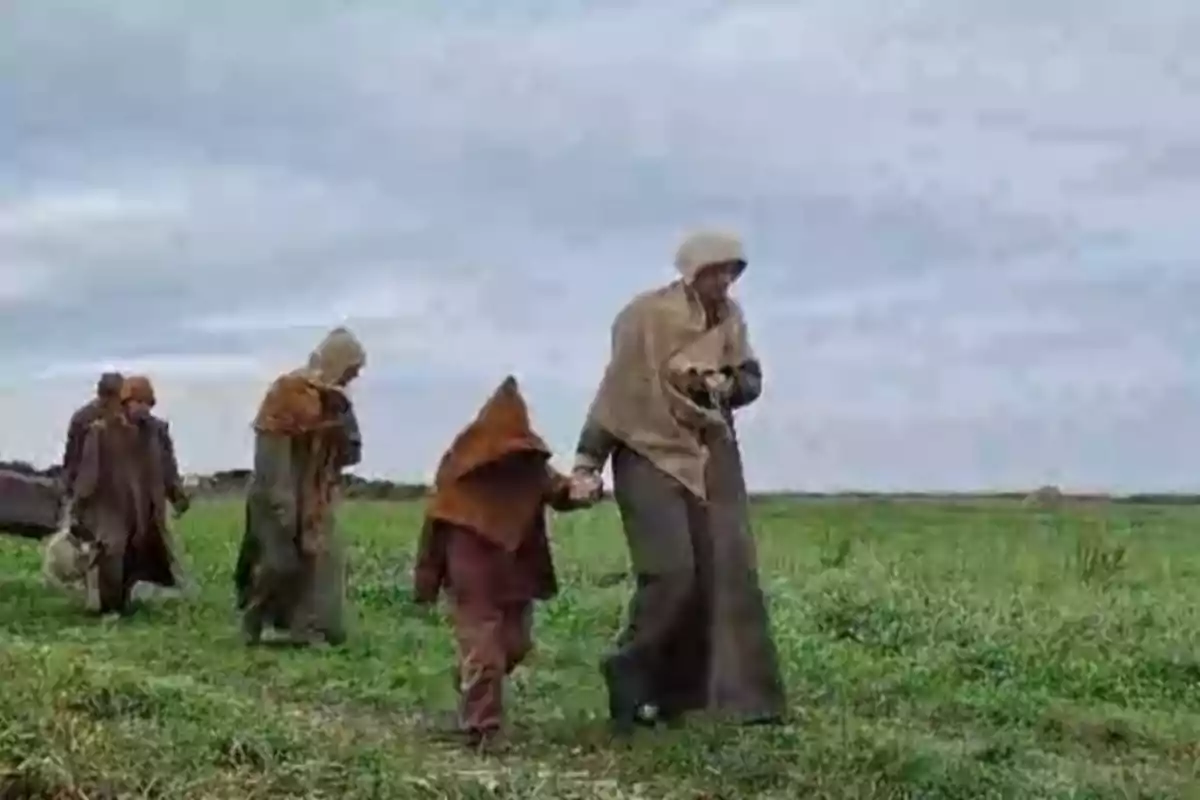 Un grupo de personas vestidas con ropas de abrigo camina por un campo verde bajo un cielo nublado.