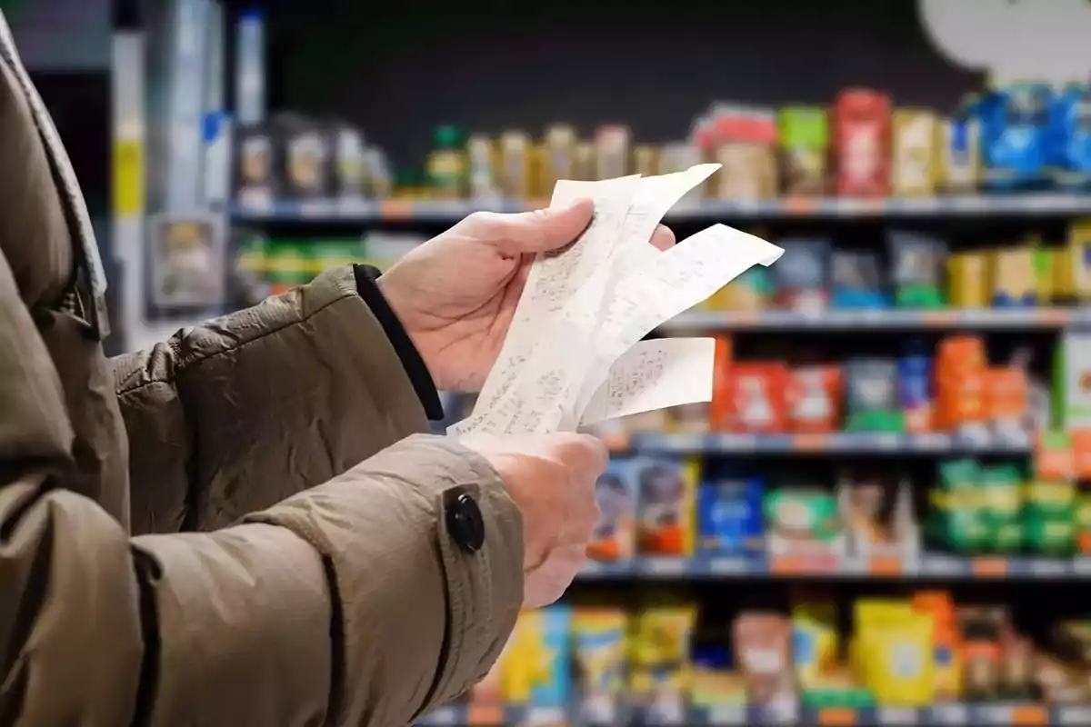 Persona revisando varios recibos en un supermercado con estantes llenos de productos al fondo.