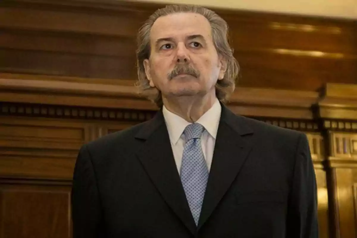 Gray-haired man with a mustache wearing a dark suit and light blue tie in a formal polished wood setting Gray-haired man with a mustache wearing a dark suit and light blue tie in a formal polished wood setting