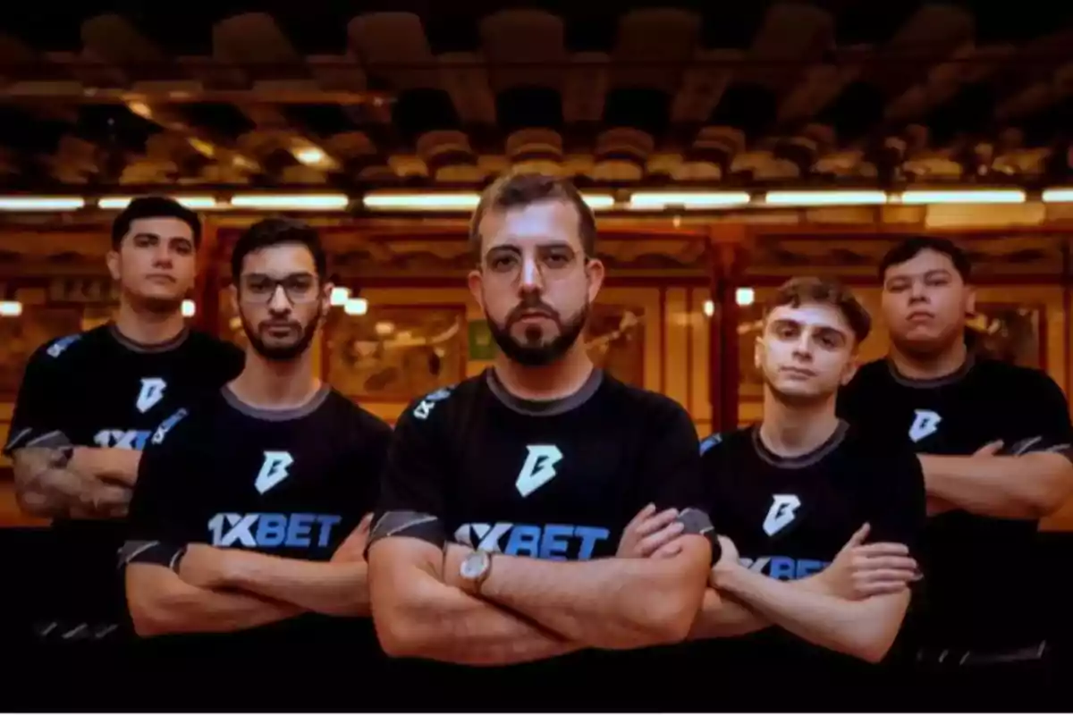 Cinco personas con camisetas negras de un equipo posan con los brazos cruzados en un entorno iluminado. Cinco personas con camisetas negras de un equipo posan con los brazos cruzados en un entorno iluminado.