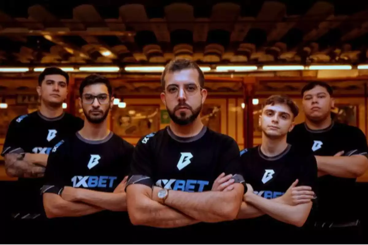 Cinco personas con camisetas negras de 1XBET posan con los brazos cruzados en un entorno interior iluminado. Cinco personas con camisetas negras de 1XBET posan con los brazos cruzados en un entorno interior iluminado.