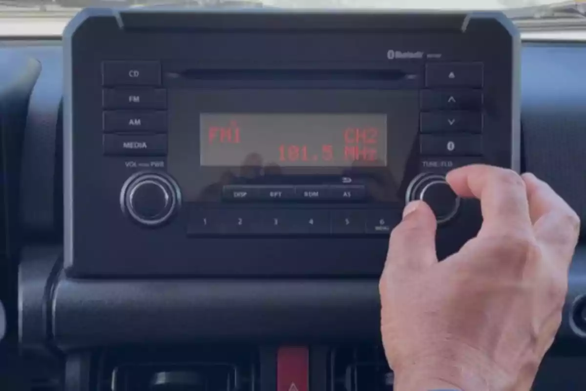 Persona ajustando la perilla de una radio de automóvil que muestra la frecuencia 101.5 MHz en la pantalla