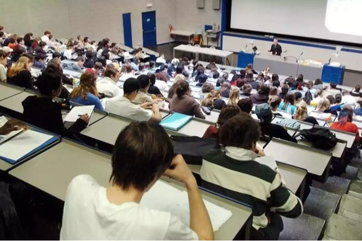 Estudiantes en un aula universitaria escuchan a un profesor durante una clase magistral.