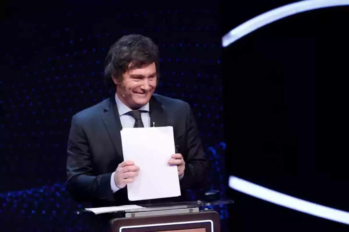 A smiling man on a stage holding papers.