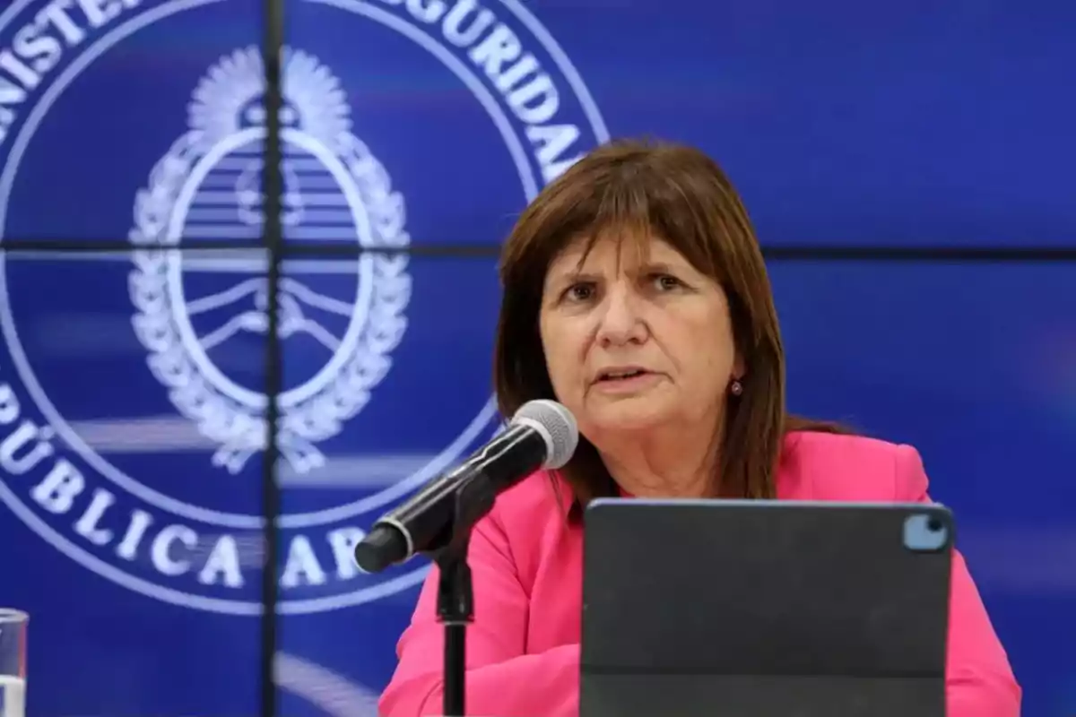 Una mujer hablando en un micrófono frente a un fondo con el logo del Ministerio de Seguridad de Argentina.