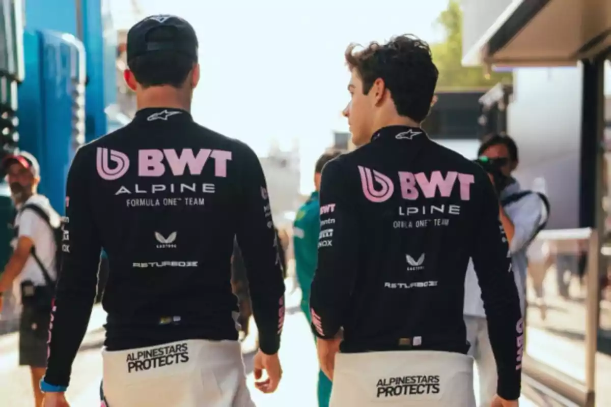 Two people in BWT Alpine uniforms walking through the paddock at a Formula 1 event. Two people in BWT Alpine uniforms walking through the paddock at a Formula 1 event.