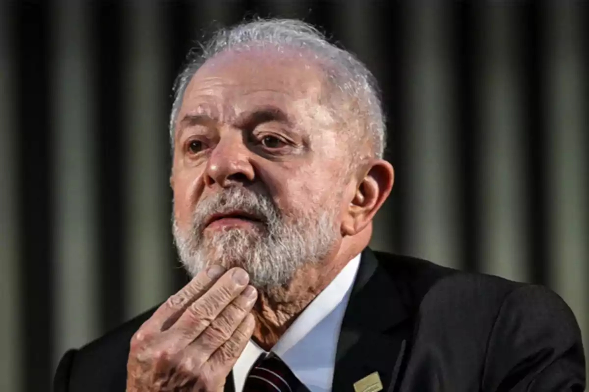 Un hombre mayor con barba blanca y traje oscuro se toca la barbilla mientras mira hacia arriba.