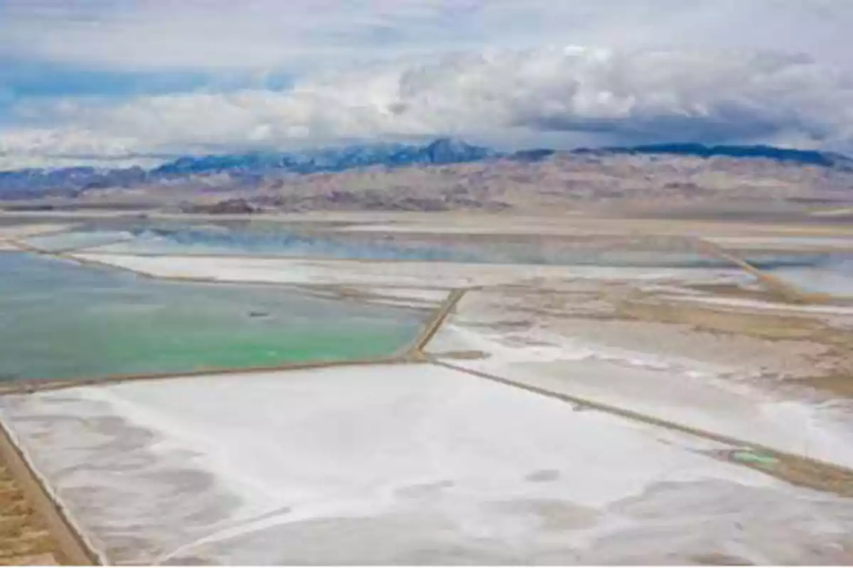 Vista aérea de un paisaje desértico con salinas y montañas al fondo bajo un cielo nublado.