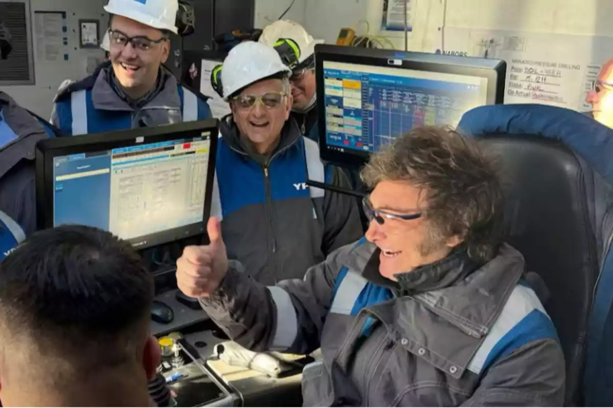 Un grupo de personas con cascos y gafas de seguridad sonríen mientras observan pantallas de computadora en un entorno industrial.