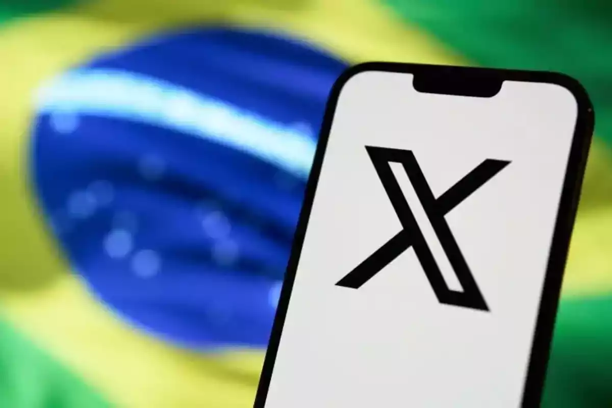 Un teléfono móvil con el logotipo de "X" en la pantalla frente a una bandera de Brasil desenfocada.