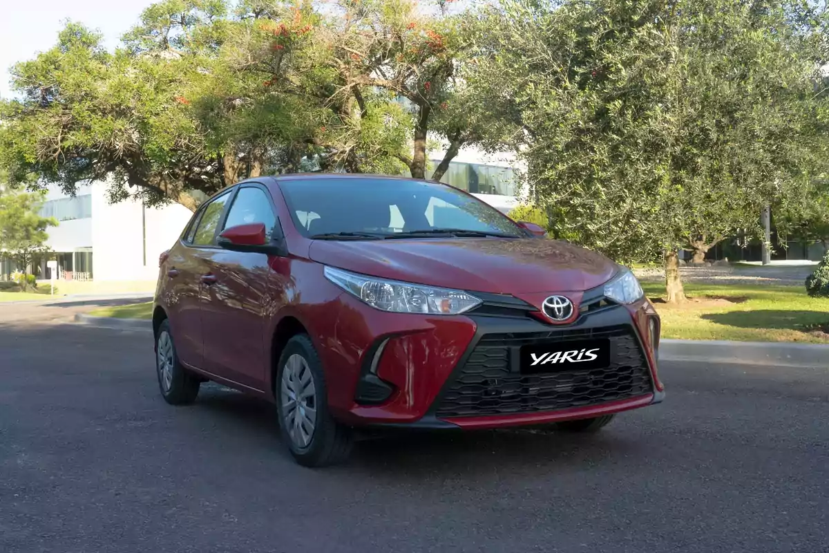 Un automóvil Toyota Yaris rojo estacionado en una calle rodeada de árboles y vegetación.