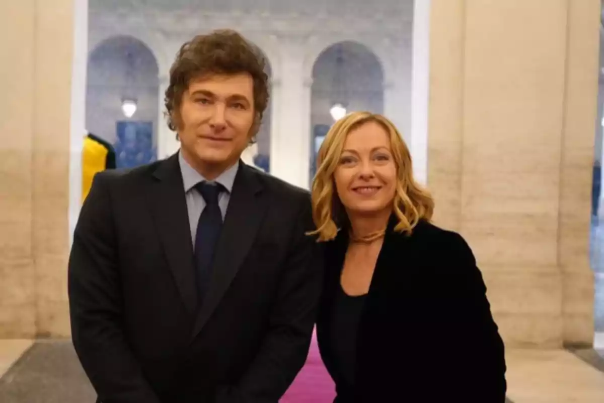 Dos personas posan sonrientes en un entorno elegante con columnas y luces al fondo