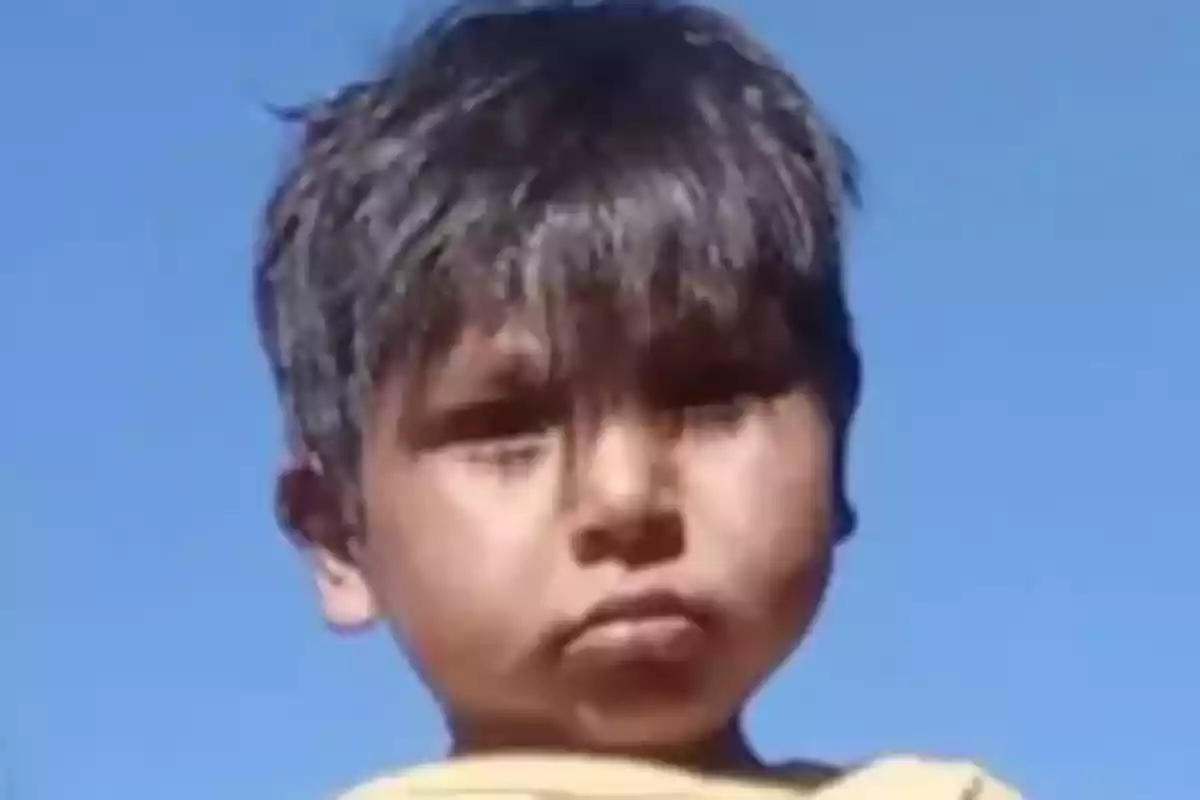 Un niño con cabello oscuro mira a la cámara con el cielo azul de fondo.