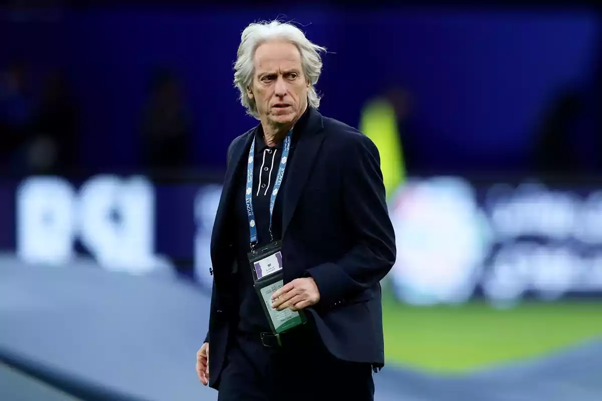 A gray-haired man in a dark suit walks through a sports stadium. A gray-haired man in a dark suit walks through a sports stadium.