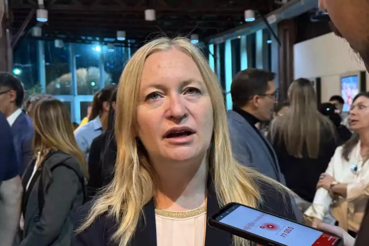 Una mujer rubia está siendo entrevistada en un evento concurrido, con personas de fondo y un micrófono cerca de su rostro. Una mujer rubia está siendo entrevistada en un evento concurrido, con personas de fondo y un micrófono cerca de su rostro.