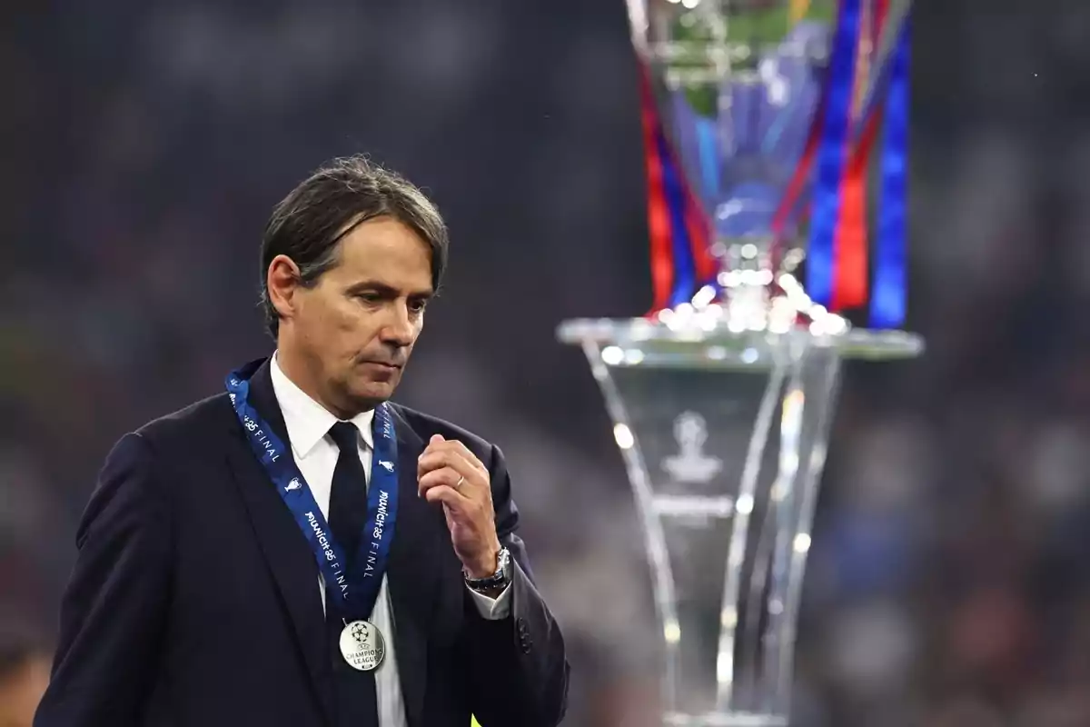 Coach with a second-place medal walks dejectedly next to the Champions League trophy.