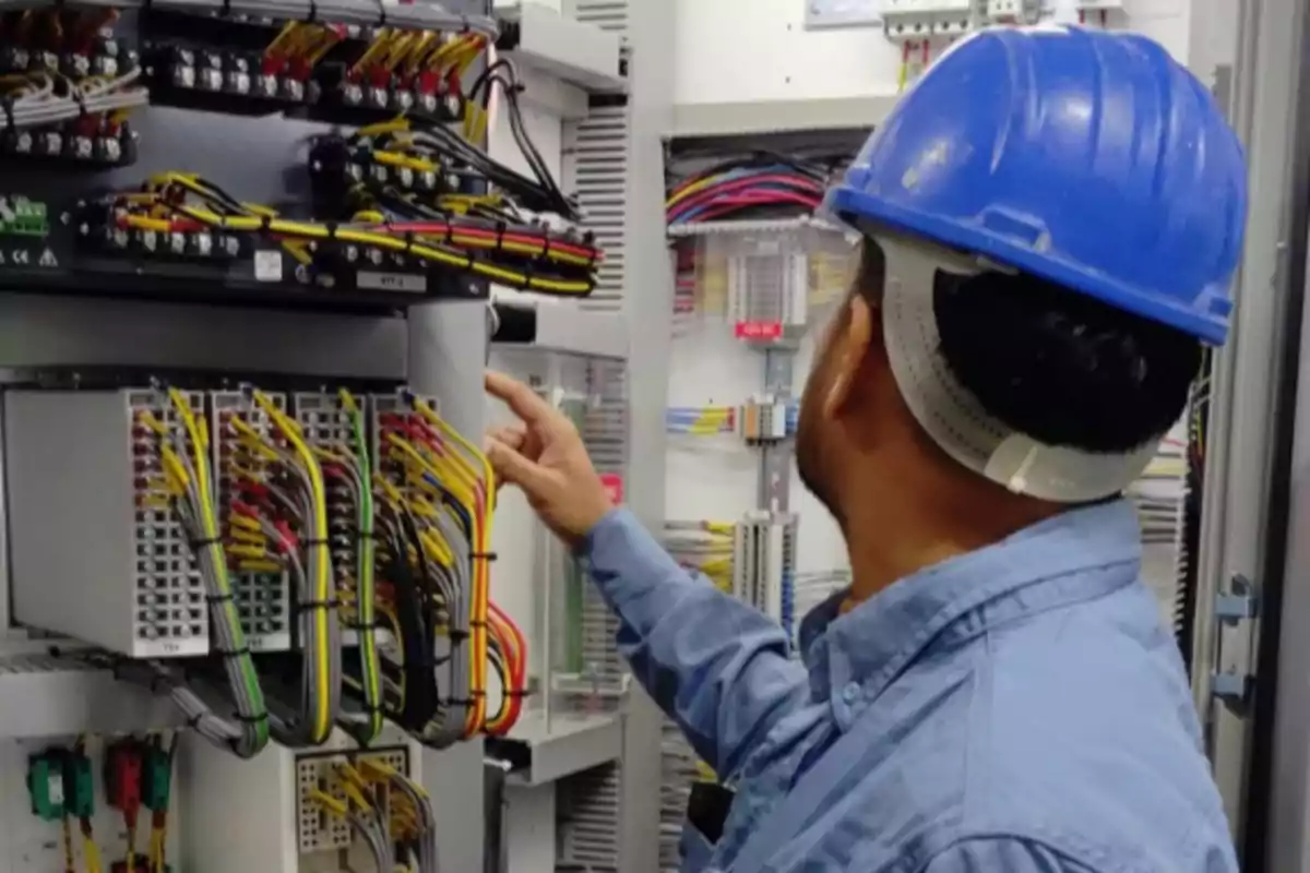 Technician with a blue helmet inspecting an electrical control panel full of colorful wires
