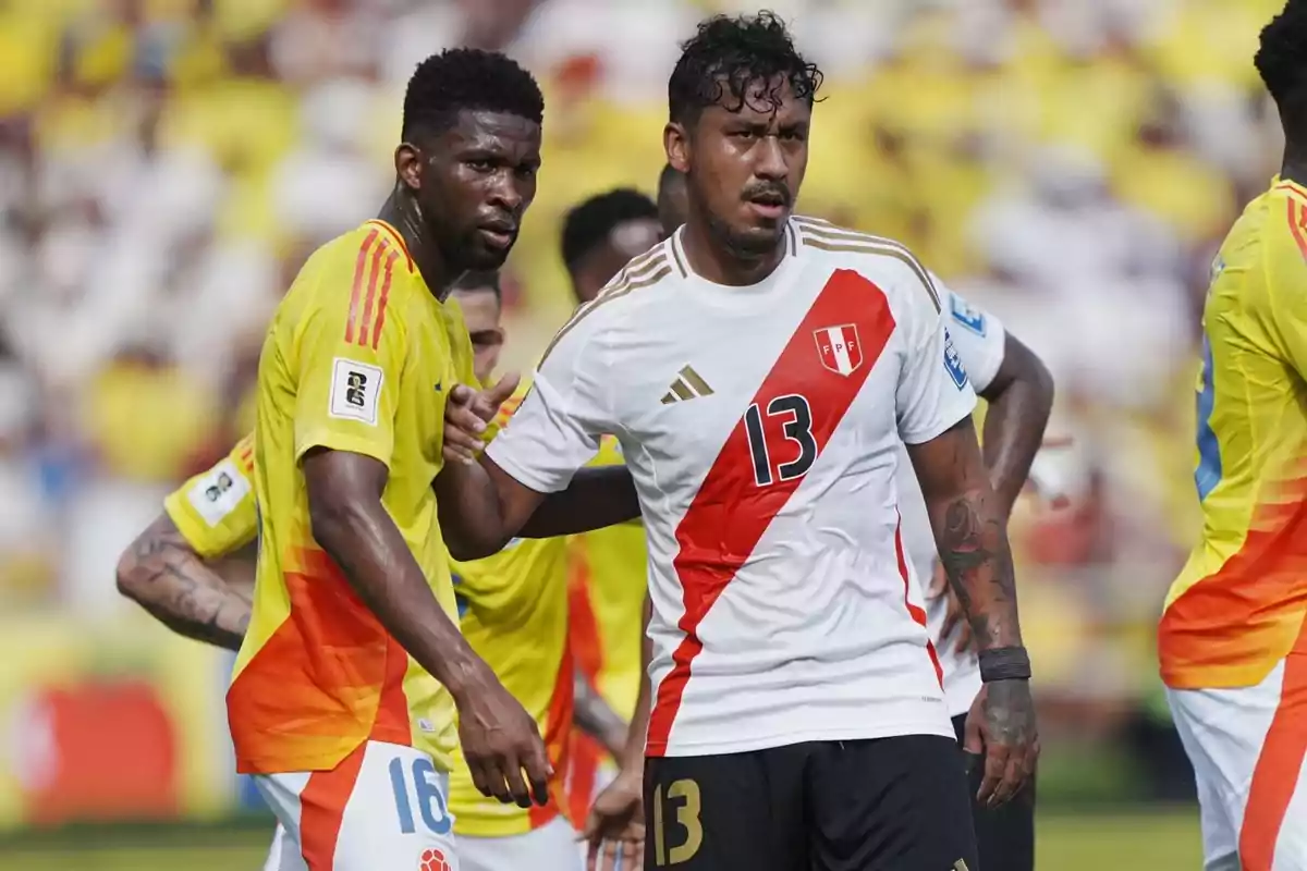 Two players from the national teams of Colombia and Peru get ready for a play during a match; both look focused, and the stadium is packed with fans in the background. Two players from the national teams of Colombia and Peru get ready for a play during a match; both look focused, and the stadium is packed with fans in the background.