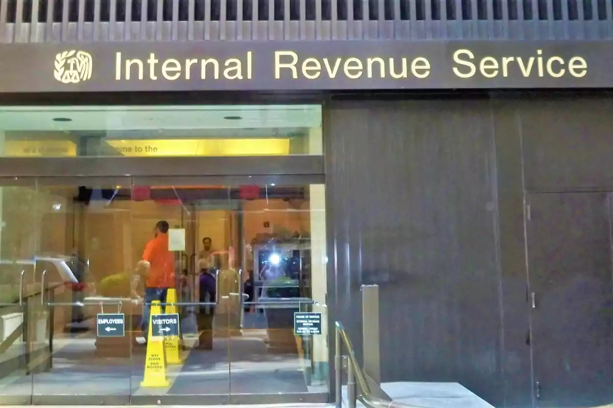 Entrance of an Internal Revenue Service building with glass doors and warning signs on the floor.