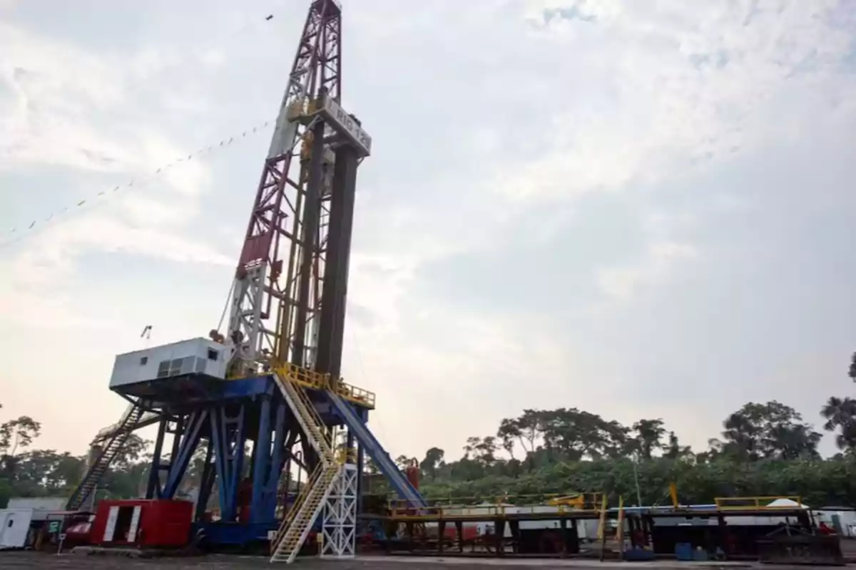 An oil drilling rig in an outdoor setting with a cloudy sky and vegetation in the background.