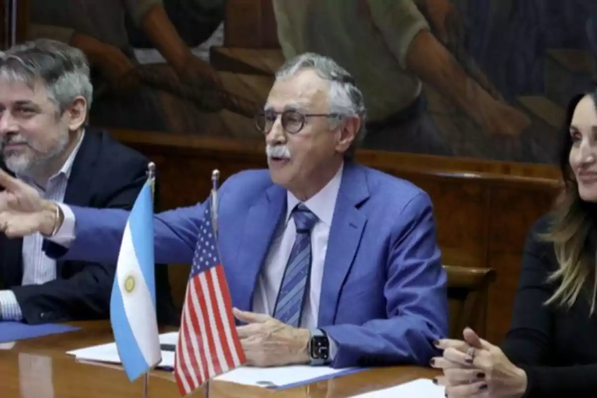 Three people sitting at a table with flags of Argentina and the United States.