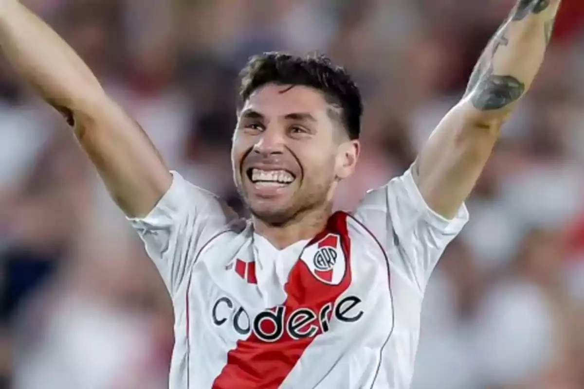 Un jugador de fútbol celebrando con los brazos en alto mientras viste la camiseta de River Plate.