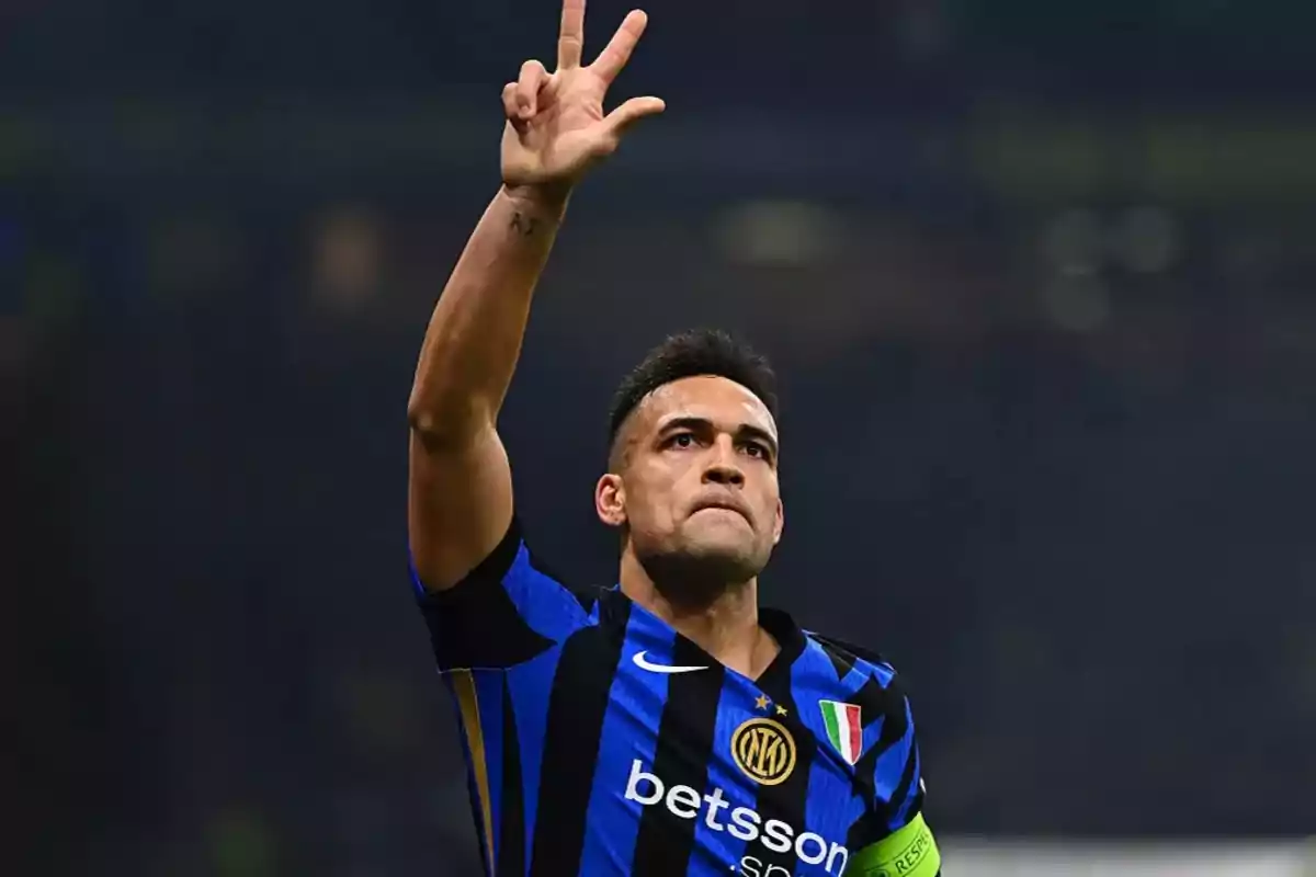 Jugador de fútbol con uniforme azul y negro levantando la mano en señal de celebración.