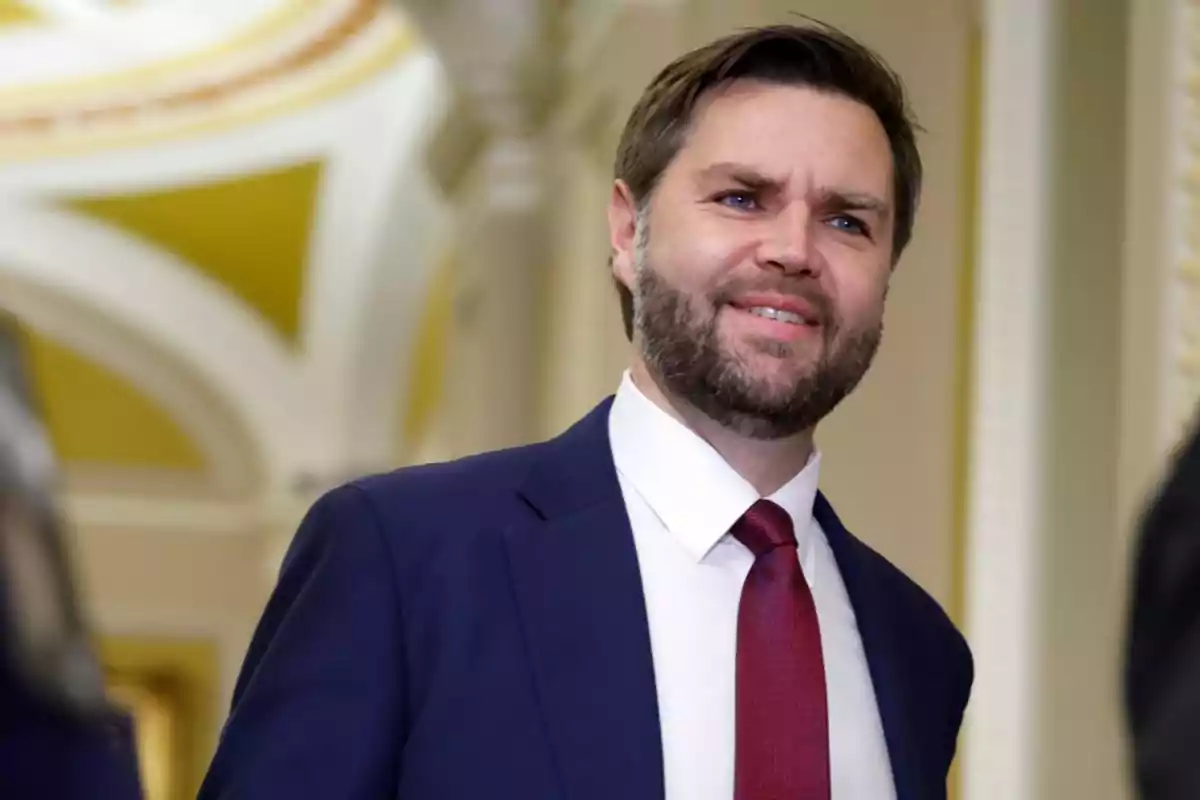 Hombre con barba y traje azul marino con corbata roja sonriendo en un edificio elegante con detalles arquitectónicos en amarillo y blanco Hombre con barba y traje azul marino con corbata roja sonriendo en un edificio elegante con detalles arquitectónicos en amarillo y blanco
