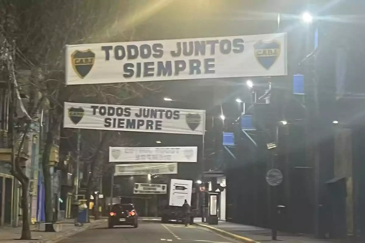 A street with several hanging signs that say "All Together Always" and have a shield with the letters "CABJ," with a car driving down the road.