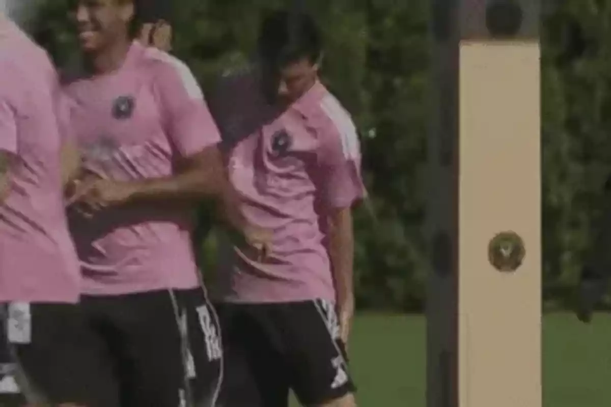 Jugadores de fútbol con uniforme rosa entrenando y uno de ellos parece golpearse accidentalmente con un poste Jugadores de fútbol con uniforme rosa entrenando y uno de ellos parece golpearse accidentalmente con un poste