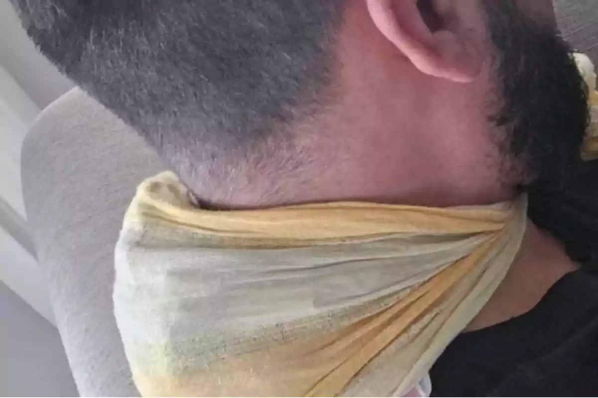 Un hombre con barba y cabello corto tiene un pañuelo amarillo alrededor del cuello mientras está sentado en un sofá.