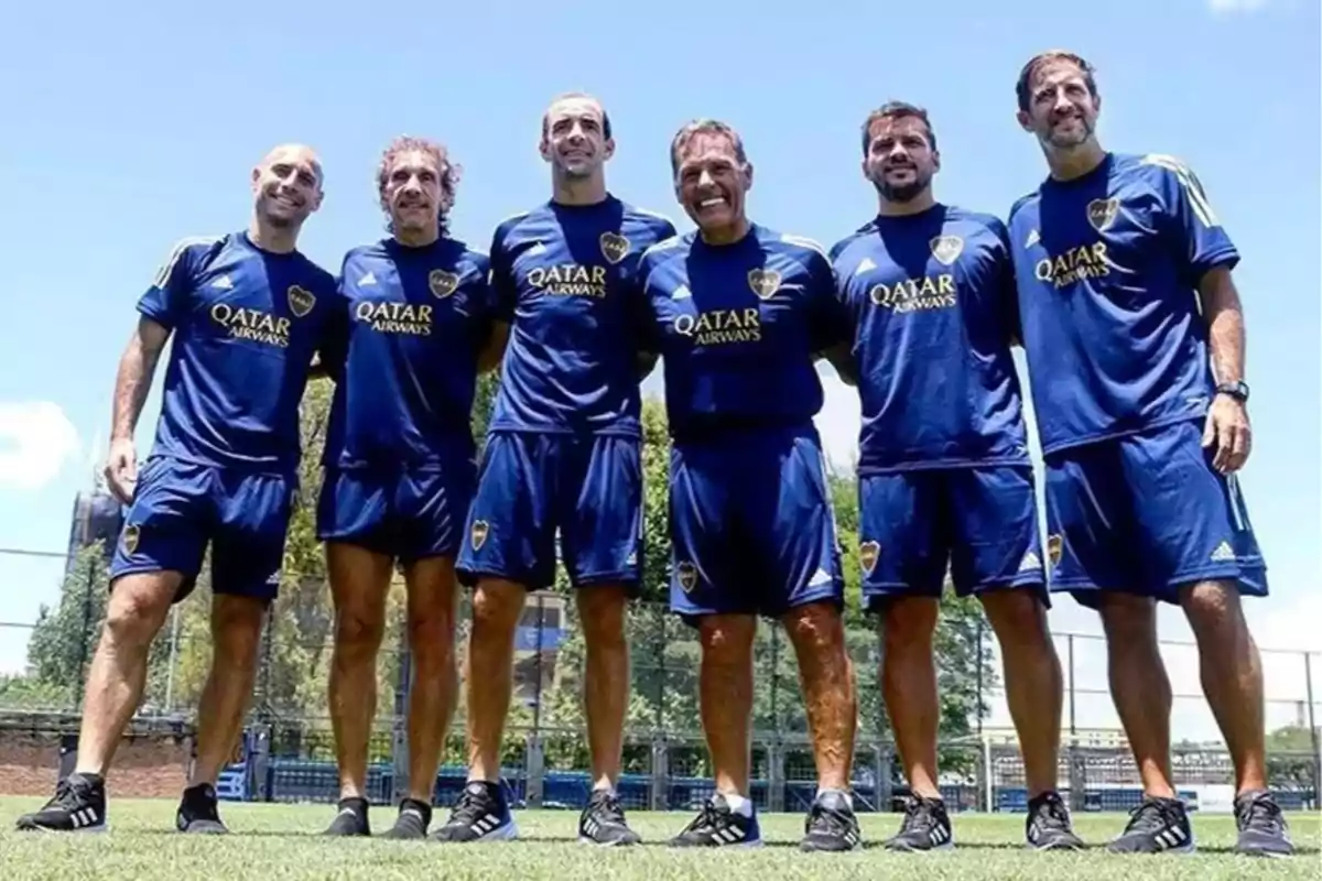 Seis hombres con uniforme azul de Boca Juniors posan sonrientes en una cancha de fútbol bajo un cielo despejado Seis hombres con uniforme azul de Boca Juniors posan sonrientes en una cancha de fútbol bajo un cielo despejado