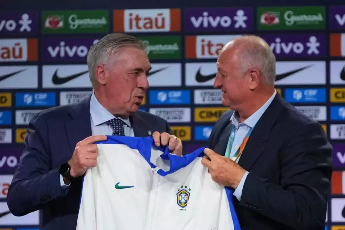 Two men in suits hold a Brazil national soccer team jacket in front of a backdrop with sponsor logos. Two men in suits hold a Brazil national soccer team jacket in front of a backdrop with sponsor logos.